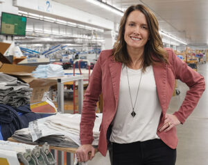 Lakeshirts Michelle Daggett poses in front of production area - Enterprise Minnesota magazine