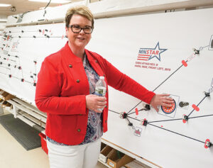 Picture of Tammy Werzal, COO of MNSTAR, standing next to a production board