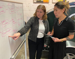 Enterprise Minnesota business growth consultant Amy Hubler reviews a marketing strategy flowchart on a whiteboard with a Vistabule team member inside the company's manufacturing facility, with a teardrop trailer visible in the background.