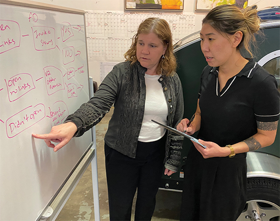 Enterprise Minnesota business growth consultant Amy Hubler reviews a marketing strategy flowchart on a whiteboard with a Vistabule team member inside the company's manufacturing facility, with a teardrop trailer visible in the background.
