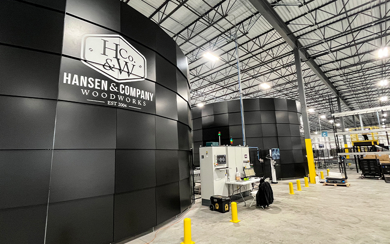 Two large cylindrical black automated storage units branded with the Hansen & Company Woodworks logo stand on the floor of the company's new 92,000-square-foot manufacturing facility in St. Joseph, Minnesota.