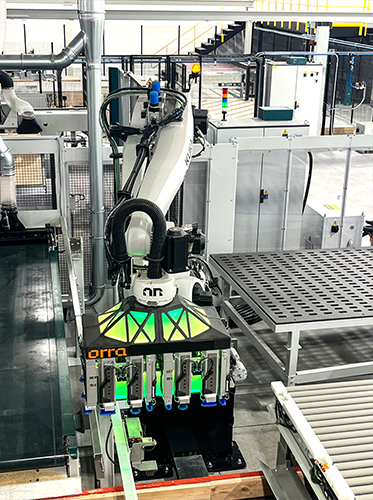 A large white KUKA robotic arm fitted with a green-illuminated Orra multi-suction end effector positions cabinet panels on the automated production line at Hansen & Co. Woodworks' St. Joseph, Minnesota facility.
