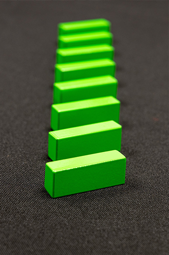 A row of bright green rectangular iron nitride magnet bricks lined up on a dark surface, fading into a soft blur in the background.