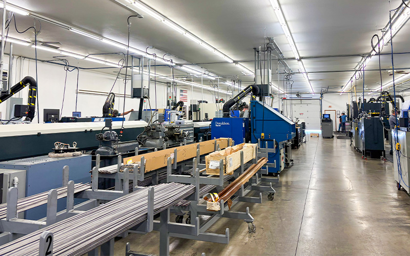 A wide view of the Wells Technology production floor in Bemidji, Minnesota, showing rows of CNC machines, metal stock racks, and employees working along a well-lit industrial space.