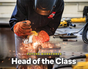 Student wearing welding gloves and face shield grinding metal in a high school shop class, sparks flying.