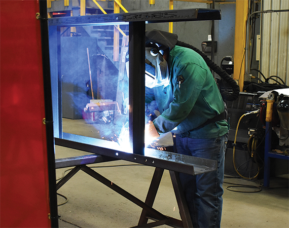 Rapat Corporation welder in protective gear welding a large steel structural frame on the shop floor.